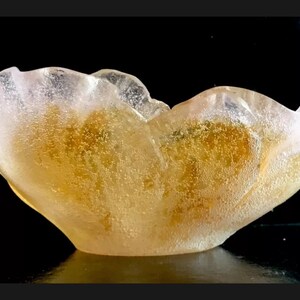 May include: A clear glass bowl with a unique, organic shape. The bowl has a light pink hue and is filled with small, golden bubbles.
