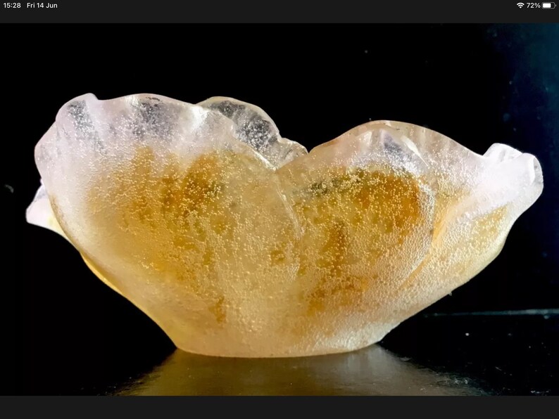 May include: A clear glass bowl with a unique, organic shape. The bowl has a light pink hue and is filled with small, golden bubbles.