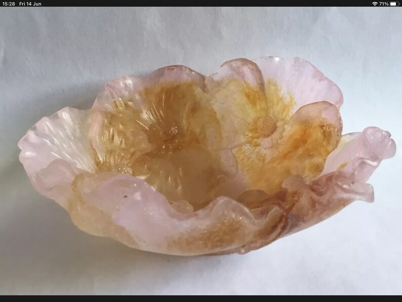 May include: A pink and gold glass bowl shaped like a flower. The bowl has a delicate, ruffled edge and a center with a raised, textured design.