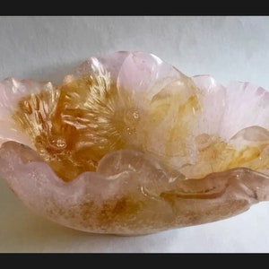 May include: A pink and amber glass bowl shaped like a flower. The bowl has a textured surface and a delicate, feminine design.