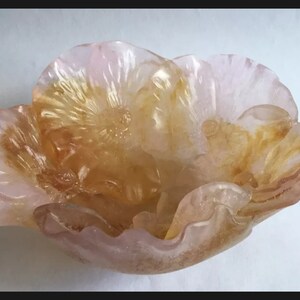 May include: A pink and gold glass flower bowl with a ruffled edge. The bowl is shaped like a flower with a center that is a darker gold color.