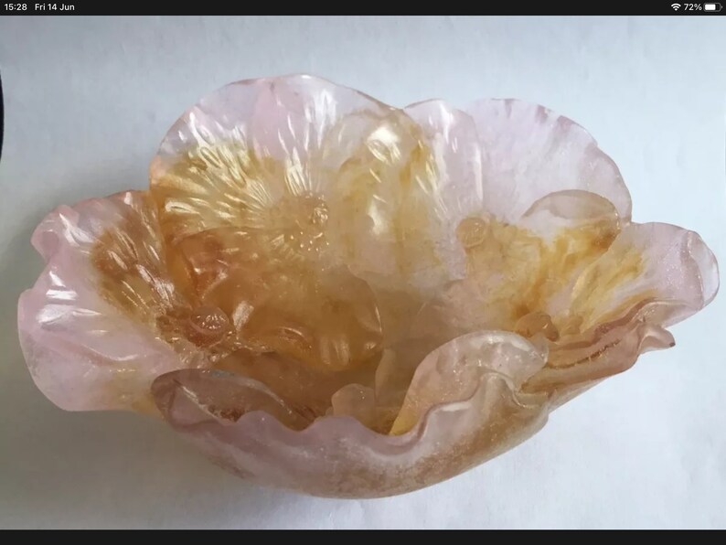 May include: A pink and gold glass flower bowl with a ruffled edge. The bowl is shaped like a flower with a center that is a darker gold color.