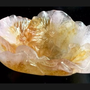 May include: A delicate, hand-carved flower bowl made of translucent pink and gold quartz. The bowl features intricate details and a delicate, feminine design.