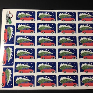 Op de afbeelding: Een vel met 25 stickers met een rode auto die een kerstboom vervoert. De auto rijdt op een besneeuwde weg met een blauwe lucht en witte sneeuwvlokken. De stickers zijn perfect om een feestelijke touch toe te voegen aan cadeaus, kaarten of andere oppervlakken.