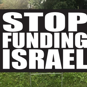 May include: A black rectangular yard sign with the words "STOP FUNDING ISRAEL" in large white capital letters. The sign is placed in a grassy yard with a metal stake.