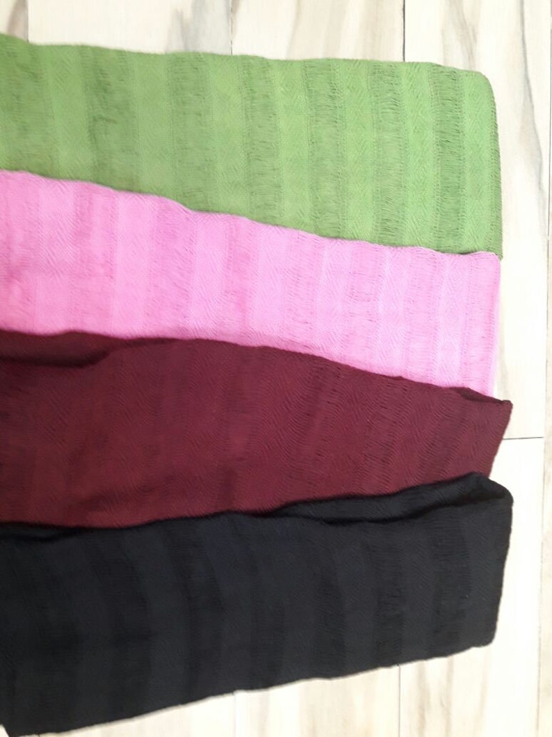 May include: Four woven scarves in different colors: green, pink, burgundy, and black. The scarves are stacked on top of each other.