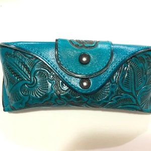 May include: Teal leather glasses case with a floral embossed design and two black snap closures.
