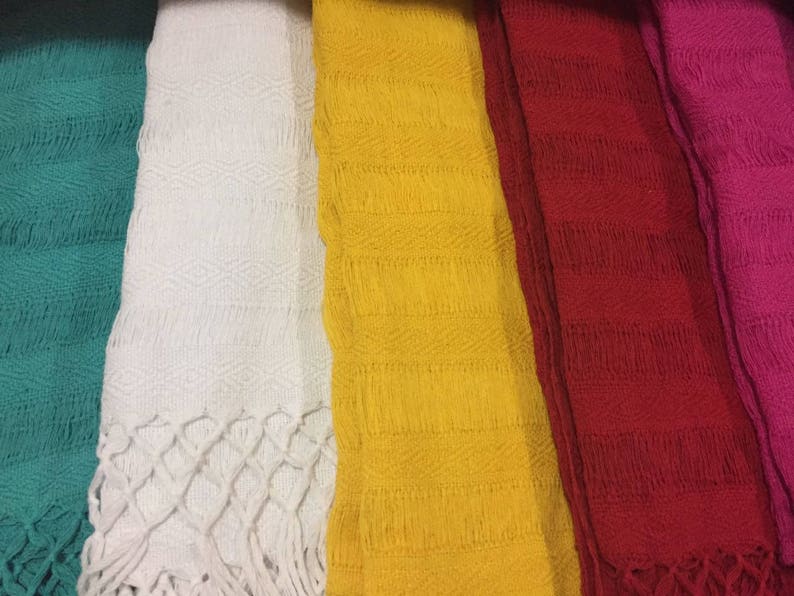 May include: Five different colored woven fabric strips with a fringe at the bottom. The colors are teal, white, yellow, red, and pink.