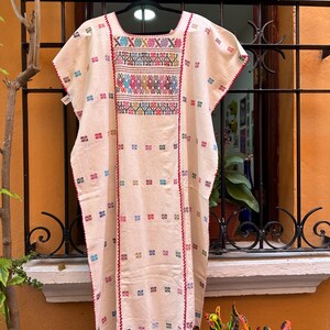 May include: A white cotton tunic with colorful embroidery. The embroidery features geometric patterns in shades of pink, blue, green, yellow, and red. The tunic has a scoop neck and short sleeves.