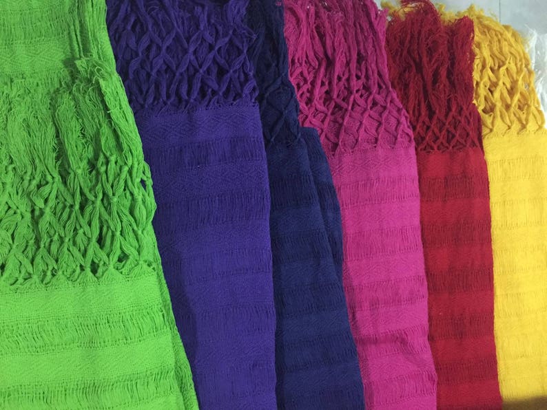 May include: A collection of colorful woven shawls with fringed edges. The shawls are arranged in a row, with the green shawl on the left and the yellow shawl on the right.