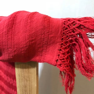 May include: A red woven shawl with a fringe border. The shawl is draped over a wooden chair.