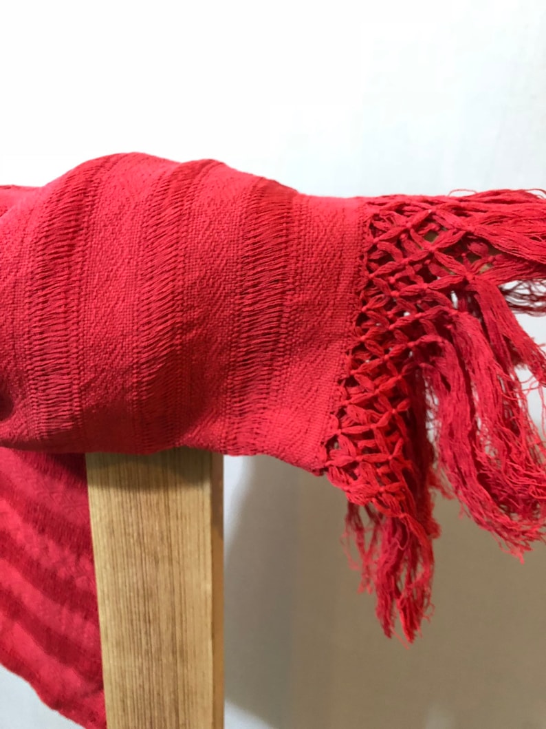 May include: A red woven shawl with a fringe border. The shawl is draped over a wooden chair.