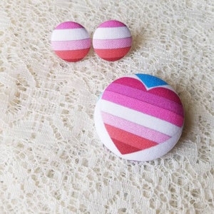May include: A set of three fabric buttons with a pink, white, and blue striped heart design. The buttons are perfect for adding a touch of personality to any project.