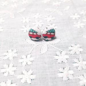 May include: A pair of red and green Christmas-themed fabric earrings with a car carrying a Christmas tree. The earrings are on a white lace background.