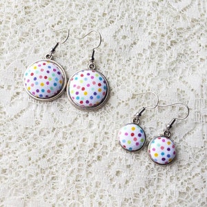 May include: A pair of colorful polka dot fabric earrings with silver hooks. The earrings are in two sizes, with the larger pair having a white background and the smaller pair having a light blue background.
