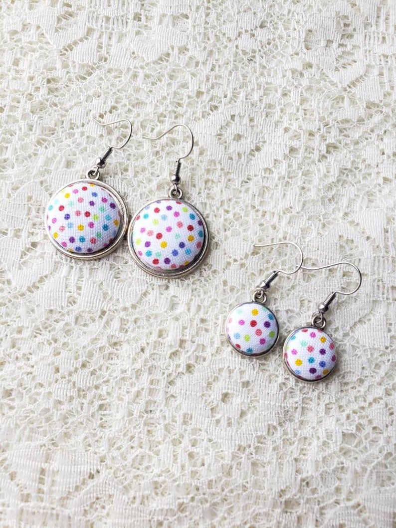 May include: A pair of colorful polka dot fabric earrings with silver hooks. The earrings are in two sizes, with the larger pair having a white background and the smaller pair having a light blue background.
