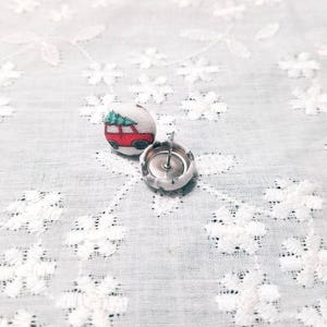 May include: A pair of fabric covered button earrings with a red car with a green Christmas tree on top. The buttons are white with a silver metal backing.