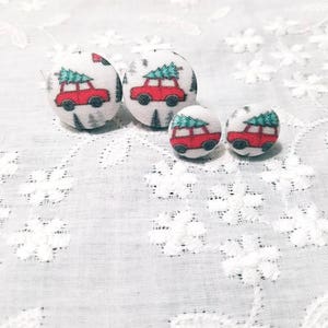 May include: Three pairs of fabric covered button earrings with a Christmas tree and car design. The buttons are white with a red car carrying a green Christmas tree on top. The buttons are different sizes.