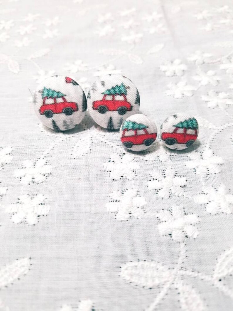 May include: Three pairs of fabric covered button earrings with a Christmas tree and car design. The buttons are white with a red car carrying a green Christmas tree on top. The buttons are different sizes.