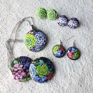 May include: A set of succulent-themed jewelry, including a necklace with a large pendant, a pair of earrings, and a pair of button earrings. The pendant and earrings feature a variety of succulents in shades of green, purple, and pink.