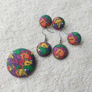 May include: A set of colorful fabric earrings and a brooch. The earrings are round and have a silver metal setting. The brooch is larger and has a similar design to the earrings.