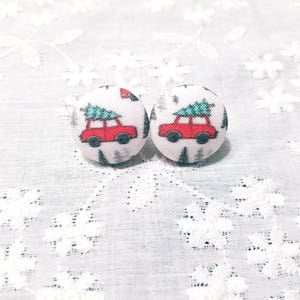 May include: A pair of Christmas-themed earrings featuring red cars carrying green Christmas trees on a white background.