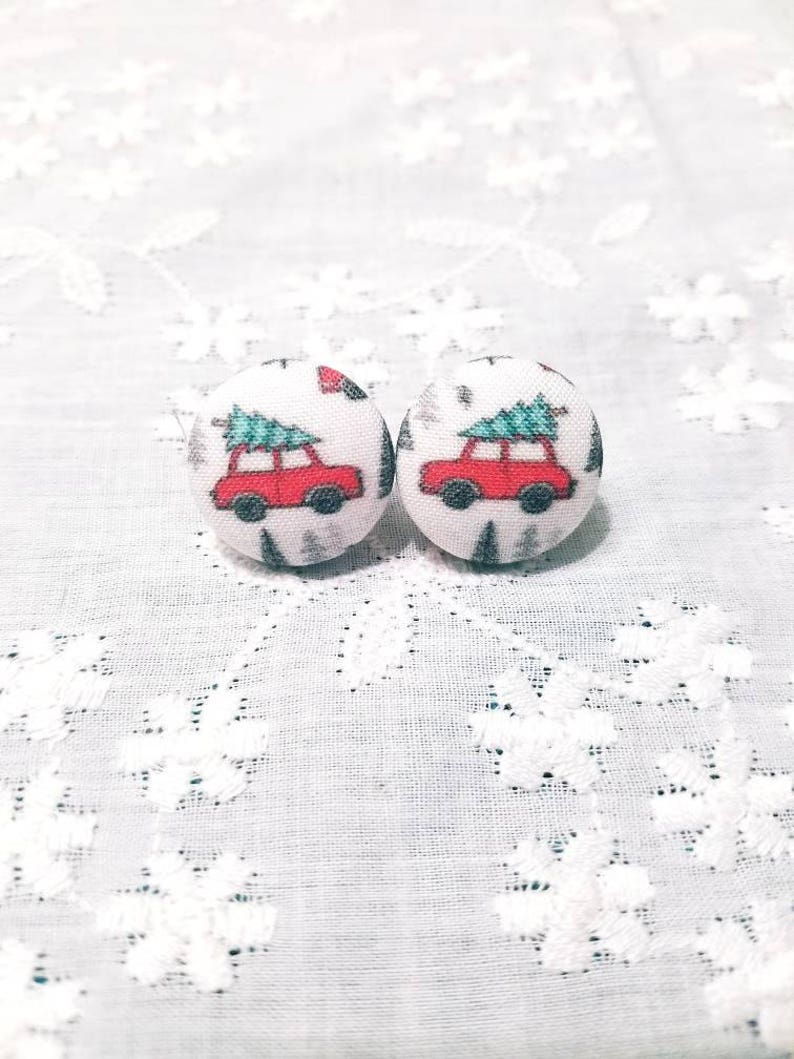 May include: A pair of Christmas-themed earrings featuring red cars carrying green Christmas trees on a white background.