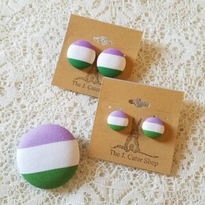 May include: A pair of purple, white, and green button earrings on a card that reads "The J. Cater Shop".