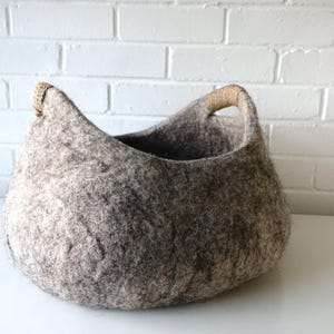 Felted wool storage basket in grey with two wrapped handles; cozy cat bed with a sleeping cat inside.