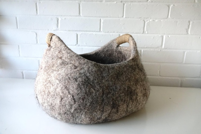 Felted wool storage basket in grey with two wrapped handles; cozy cat bed with a sleeping cat inside.