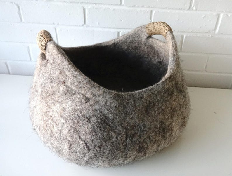 Felted wool storage basket in grey with two wrapped handles; cozy cat bed with a sleeping cat inside.