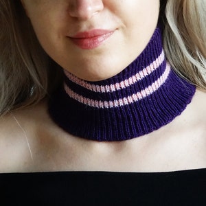 Könnte beinhalten: Ein lila gestrickter Halsschmuck mit zwei rosa Streifen.