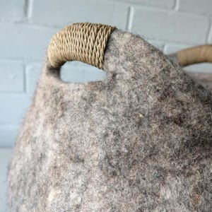 Felted wool storage basket in grey with two wrapped handles; cozy cat bed with a sleeping cat inside.