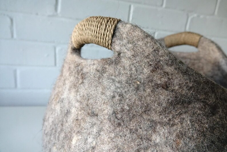 Felted wool storage basket in grey with two wrapped handles; cozy cat bed with a sleeping cat inside.