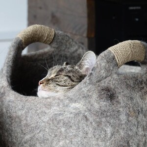 Felted wool storage basket in grey with two wrapped handles; cozy cat bed with a sleeping cat inside.