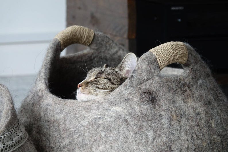 Felted wool storage basket in grey with two wrapped handles; cozy cat bed with a sleeping cat inside.