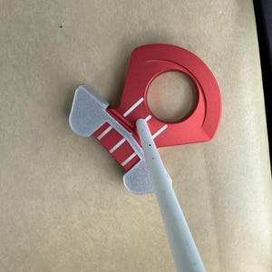 May include: Red and silver metal tool with a circular opening and a pointed white object. The tool has a red body with white stripes and a silver section. The white object is long and cylindrical.