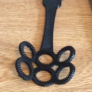 May include: Black plastic toy with a handle and five circular openings. The toy is shaped like a flower with five petals.