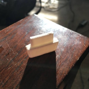 Puede incluir: Una pequeña figura de barco de plástico blanco. El barco tiene un fondo plano y una cubierta elevada con una pequeña barandilla.