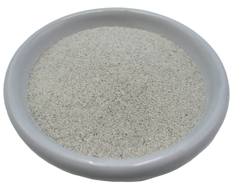 May include: A white, shallow, round ceramic bowl filled with a light gray, granular substance. The bowl has a slightly raised rim and sits against a white background. The granular material appears to be fine and evenly distributed.