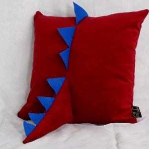 May include: Red velvet pillow with a blue felt dinosaur tail. The tail is made of several blue felt triangles.