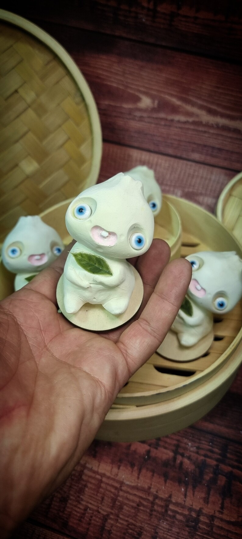 Puede incluir: Cuatro figuritas de cer&aacute;mica blanca con grandes ojos azules y mejillas rosadas. Las figuritas tienen forma de alb&oacute;ndigas y sostienen hojas verdes. Las figuritas est&aacute;n sentadas en una vaporera de bamb&uacute;.