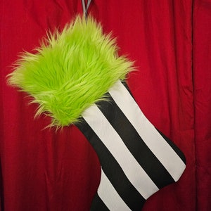 May include: A black and white striped Christmas stocking with a green fuzzy top. The stocking has a loop at the top for hanging.