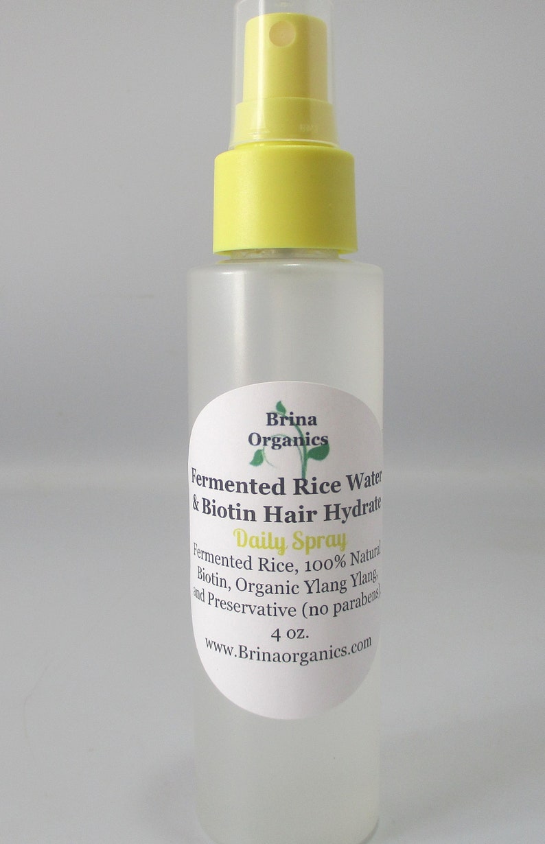 K&ouml;nnte beinhalten: Eine durchsichtige Kunststoffspr&uuml;hflasche mit gelbem Spr&uuml;hkopf, die Brina Organics Fermented Rice Water & Biotin Hair Hydrate enth&auml;lt. Das Etikett listet Inhaltsstoffe wie fermentierten Reis, Biotin und Bio-Ylang-Ylang auf.