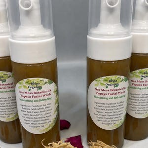 May include: Four clear plastic pump bottles containing amber-colored Sea Moss Botanical & Papaya Facial Wash. Each bottle features a white label with green leaf graphics, listing ingredients like Caribbean Sea Moss, White Willow Bark, and Papaya.