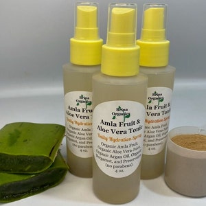 May include: Three 4-ounce bottles of Amla Fruit & Aloe Vera Tonic Daily Hydration Spray by Brina Organics. The bottles are clear with yellow spray tops and white labels. The label text reads "Amla Fruit & Aloe Vera Tonic Daily Hydration Spray" and lists the ingredients: Organic Amla Fruit, Organic Aloe Vera Juice, Organic Argan Oil, Organic Bergamot, and Preservatives (no parabens).