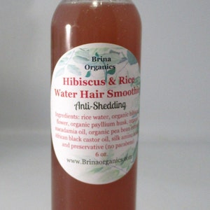 May include: A clear plastic bottle containing a reddish-brown liquid hair product with a white cap. The label reads Brina Organics Hibiscus & Rice Water Hair Smoothie Anti-Shedding, listing ingredients and a 6 oz. volume, with a green leaf design.