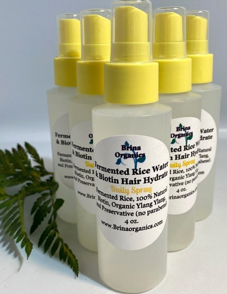 K&ouml;nnte beinhalten: F&uuml;nf durchsichtige Kunststoff-Spr&uuml;hflaschen mit gelben Pumpk&ouml;pfen, jede mit einem wei&szlig;en ovalen Etikett. Die Etiketten tragen die Aufschrift Brina Organics Fermented Rice Water & Biotin Hair Hydrate Daily Spray, 4 oz., und listen Inhaltsstoffe wie Reiswasser auf.