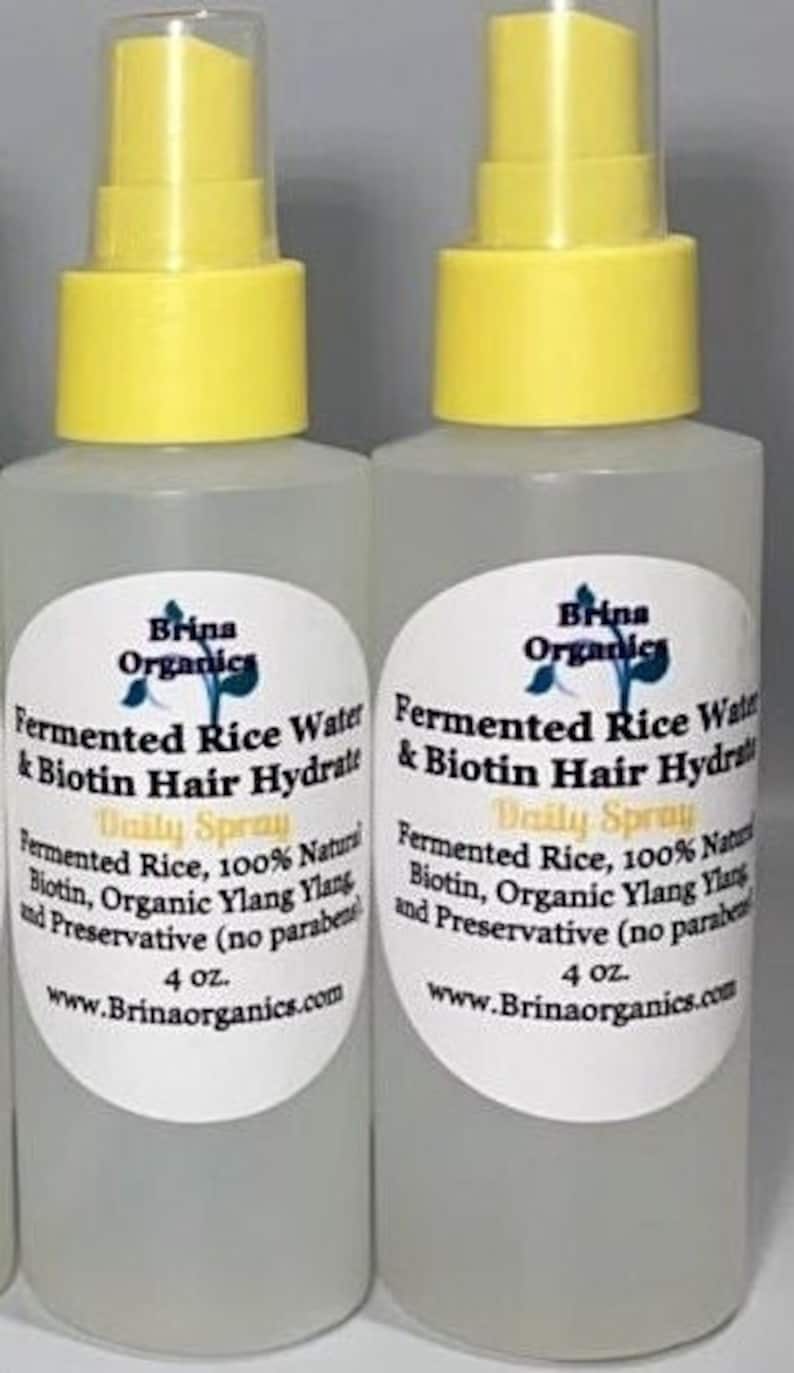 K&ouml;nnte beinhalten: Zwei durchsichtige Kunststoff-Spr&uuml;hflaschen mit gelben Kappen, die jeweils 118 ml Brina Organics Fermented Rice Water & Biotin Hair Hydrate Daily Spray enthalten. Die wei&szlig;en ovalen Etiketten f&uuml;hren Inhaltsstoffe wie Reiswasser auf.