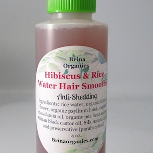 May include: A clear plastic squeeze bottle with a bright green cap containing a pink liquid. The label reads Brina Organics Hibiscus & Rice Water Hair Smoothie, Anti-Shedding, listing ingredients and 4 oz. volume, with a botanical leaf design.